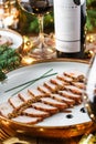 Holiday dish of sliced baked meat with sauce in plate on wooden table served with plate, glasses, bottle of wine, candles, fir Royalty Free Stock Photo