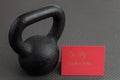 Holiday fitness, black kettlebell, with a red valentine card, on a black gym floor