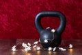 Holiday fitness, black kettlebell with white snowflake twinkle lights, against a red background