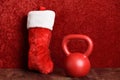 Holiday fitness, red kettlebell, red and white plush Christmas stocking against a red background`