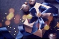 Holiday gift box or present with blue ribbon, golden confetti, baubles and light blur bokeh on black background. Christmas greetin Royalty Free Stock Photo