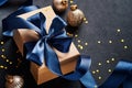 Holiday gift box or present with blue ribbon, golden confetti and gold baubles on black background. Magic christmas greeting card. Royalty Free Stock Photo