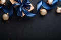 Holiday gift box or present with blue ribbon, golden confetti and gold baubles on black background. Magic christmas greeting card. Royalty Free Stock Photo