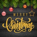 Holiday gift card with golden hand lettering Merry Christmas and Christmas balls, fir tree branches on wood background Royalty Free Stock Photo