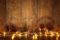 Holiday image with Christmas golden garland lights and pine cones over wooden background