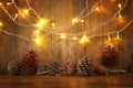 Holiday image with Christmas golden garland lights and pine cones over wooden background