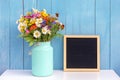 Holiday mock up. Empty blank black letter board and bouquet of bright flowers in tin can vase on table against blue Royalty Free Stock Photo