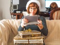 Young woman with stacked gifts looking at tablet on couch