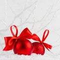 Holiday New Year background with two shine glitter glossy red balls with bright scarlet ribbon in white decorative snow, frosty. Royalty Free Stock Photo