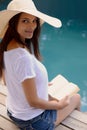 Holiday, portrait and woman at pool with book, hat and relax with happy summer travel on hotel patio. Vacation, deck and Royalty Free Stock Photo