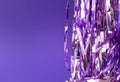 Holiday tinsel on violet background, horizontal. Creative backdrop