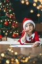 A little girl concentrated on her wish list for Santa, a New Year tree in the background