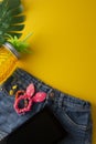 Holiday, summer background. Jeans, palm leaves, tablet screen, pineapple glass juicer. Colorful styled flat lay, yellow background