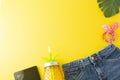 Holiday, summer background. Jeans, palm leaves, tablet screen, pineapple glass juicer. Colorful styled flat lay, yellow background