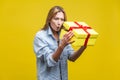 Holiday surprise. Portrait of astonished curious woman in denim shirt looking inside gift box. studio shot on yellow