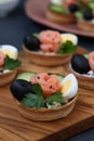 Holiday tartlets with cheese, salmon, black olives, quail eggs and cucumbers on wooden board on dark background, Vertical Royalty Free Stock Photo