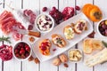 Holiday themed appetizer table spread with assorted cheeses, meats and crostini, above view over white wood