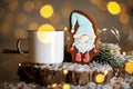 Holiday traditional food bakery. Gingerbread little fairytale gnome in cozy decoration with garland lights and cup of hot coffee