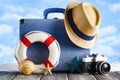 Holiday travel concept - suitcase, summer hat, photo camera, lifebuoy and shells on beach and wooden background Royalty Free Stock Photo