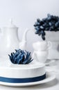 Holiday white mousse cake decorated with blue creative flower with tea set and grape on stand cake on background. Vertical Food