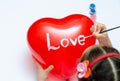 For the holiday, a 5-year-old girl writes the word love with white paint on a heart-shaped balloon. Blurry, defocused, selective Royalty Free Stock Photo