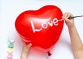 For the holiday, a 5-year-old girl writes the word love with white paint on a heart-shaped balloon. Blurry, defocused, selective Royalty Free Stock Photo
