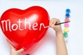 For the holiday, a 5-year-old girl writes the word mom with white paint on a heart-shaped balloon. Blurry, defocused, selective Royalty Free Stock Photo