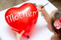 For the holiday, a 5-year-old girl writes the word mom with white paint on a heart-shaped balloon. Blurry, defocused, selective Royalty Free Stock Photo