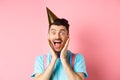 Holidays and celebration concept. Close-up of funny guy in birthday hat shouting surprised, screaming with joy