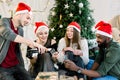 Holidays and celebration concept - happy friends in santa hats having christmas party at cozy decorated home, drinking Royalty Free Stock Photo