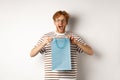 Holidays and celebration concept. Surprised redhead man receiving present inside shopping bag, looking amazed and Royalty Free Stock Photo