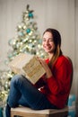 Holidays, celebration and people concept - smiling woman wearing red sweather and jeans holding gold gift box over Royalty Free Stock Photo