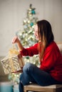 Holidays, celebration and people concept - smiling woman wearing red sweather and jeans holding gold gift box over Royalty Free Stock Photo