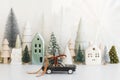 Holidays are coming! Stylish little car carrying christmas tree on background of Christmas miniature snowy village. Merry