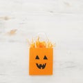 Holidays image of Halloween. Shopping orange bag with funny face over white wooden background. top view, flat lay