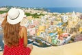 Holidays in Italy. Back view of beautiful girl with hat on wall looking at stunning sight of Procida Island, Naples, Italy