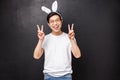 Holidays, party and Easter concept. Cheerful asian cute guy in rabbit ears and glasses showing peace signs, looks kawaii