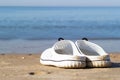 Holidays at sea. White sea slippers on the golden sand near the sea water. The best idea for a summer vacation.