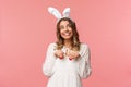 Holidays, spring and party concept. Cute romantic young blond girl imitating bunny, wear white dress lovely rabbit ears