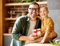 Excited boy son giving gift box for young loving father on holiday while sitting together on sofa Royalty Free Stock Photo