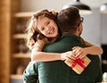 Excited girl daughter giving gift box for young loving father on holiday while hugging together on sofa Royalty Free Stock Photo