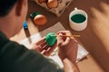 Holidays, tradition and people concept - close up of man hands coloring easter eggs with brush