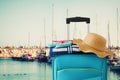Holidays. travel concept. blue suitcase with female hat, flip flips and beach towel in front of marina with yachts background
