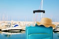 Holidays. travel concept. blue suitcase with female hat, sunglasses in front of tropical marina background Royalty Free Stock Photo