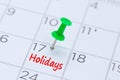 Holidays written on a calendar with a green push pin to remind y