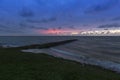 Holland - Sunset over the stormy sea. A stone rampart jutting out into the sea. in the foreground sand and green grass Royalty Free Stock Photo