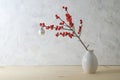 Holly or ilex branch with red berries and a white Christmas ball in a small vase against a plastered wall, simple but effectual