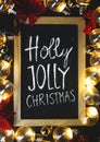 Holly Jolly Christmas Typography on Blackboard Between Light Bulbs and Red Poinsettia on Black Wood