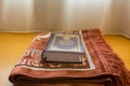 A holly Quran book on a traditional Arabic carpet at the window under sunlight at the room of hotel