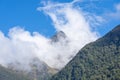 Hollyford River Valley between mountains and peaks with low cloud against blue sky